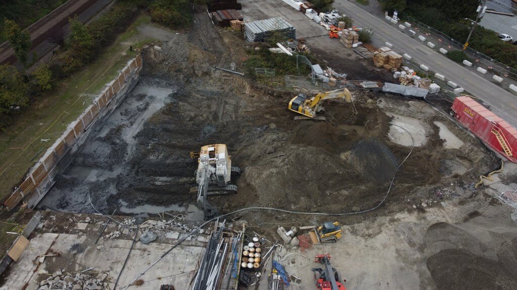 A drone image of the Cantera site during construction. Dirt piles and excavation equipment fill the image, bordered by grass on the left and a road on the right