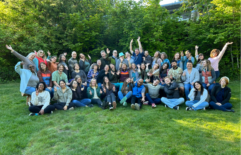 Group photo of Floyd|Snider staff posed on a grassy area with trees in the background. Staff were encouraged to be silly in the photo.