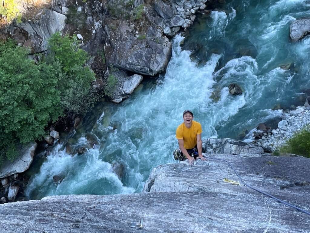 Gabe hanging from a rock wall in a yellow shirt above the river